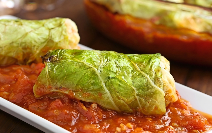 Vegetarische Kohlroulade gefüllt mit Reis, Paprika, Zwiebel und Karotte, serviert auf Tomatensauce, fotografiert mit natürlichem Licht (Selektiver Fokus, Fokus auf die Vorderseite der Roulade)