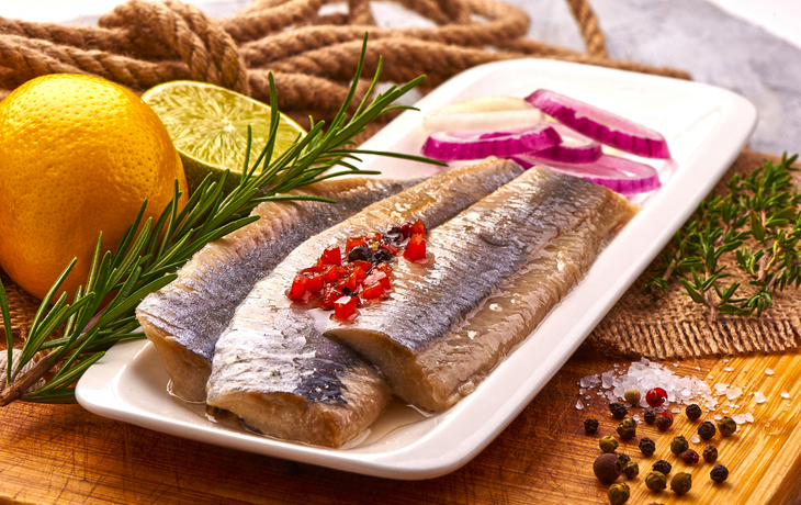 mariniertes Heringsfilet mit Pfeffer, Tomaten, Kräutern, Zwiebenl und Zitrone auf Schneidebrett