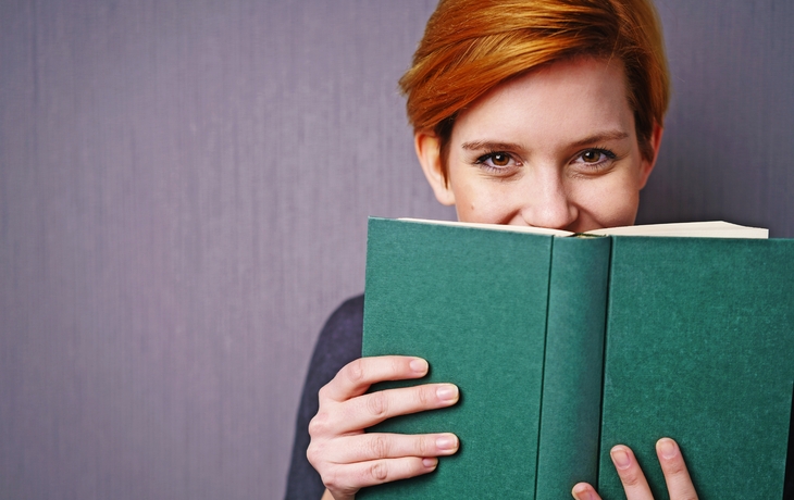 lachende frau versteckt sich hinter einem buch