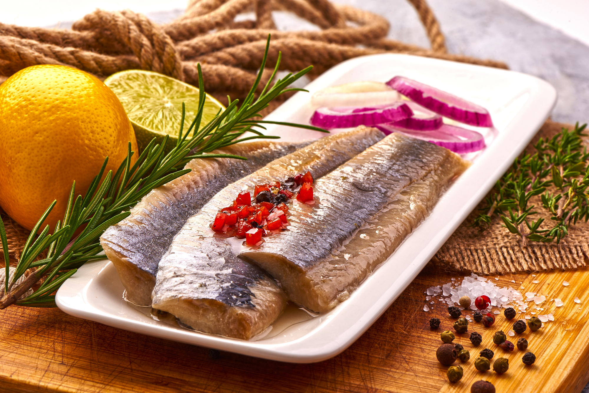 mariniertes Heringsfilet mit Pfeffer, Tomaten, Kräutern, Zwiebenl und Zitrone auf Schneidebrett