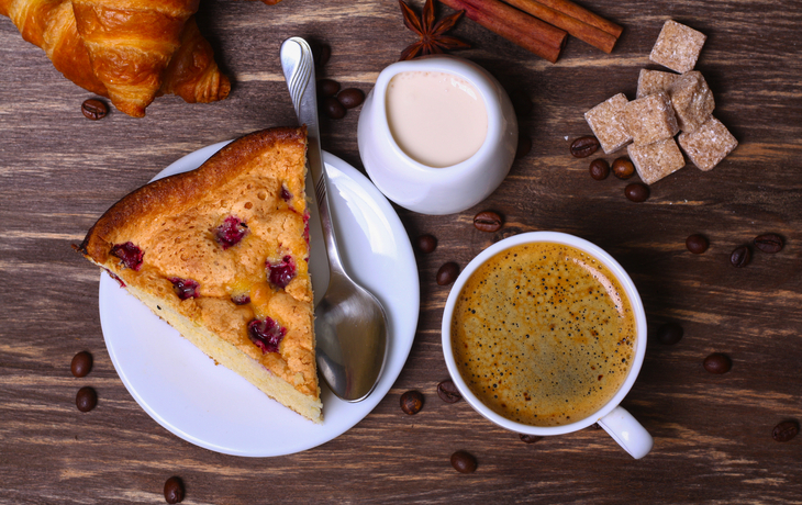 Tasse Kaffee mit Kuchen mit Cranberries und Croissants auf einem hölzernen Hintergrund